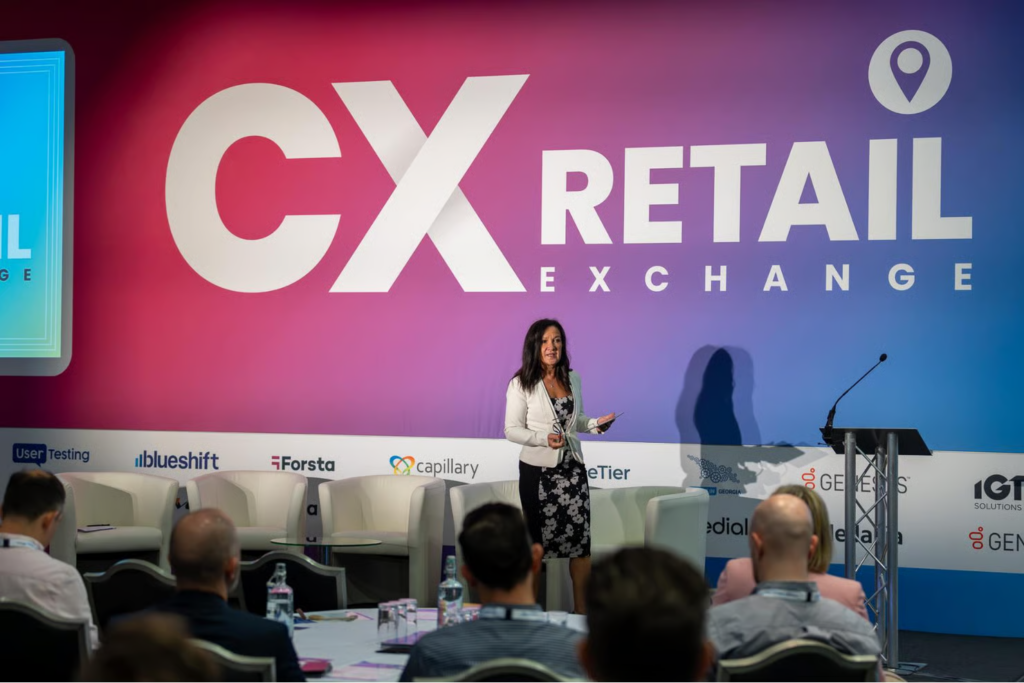 Woman presenting on stage at CX Retail Exchange conference before a seated audience.