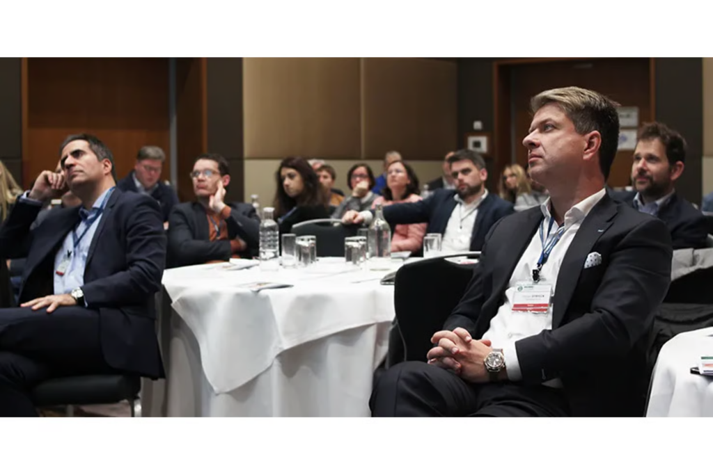 Professionals seated at round tables listening attentively at a business conference.